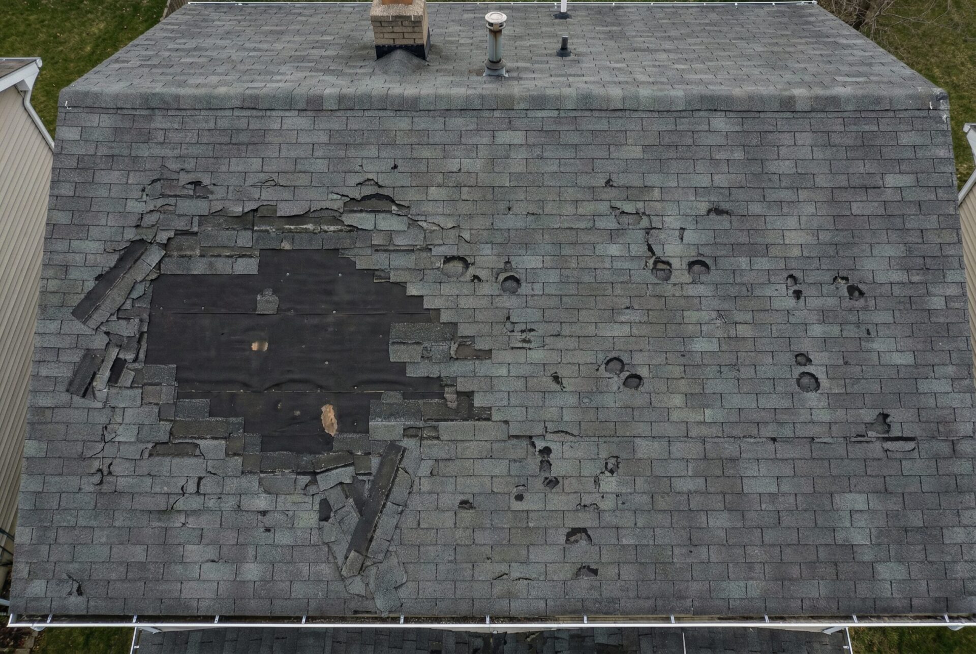 Aerial drone view of storm damage on a residential asphalt shingle roof showing missing and damaged shingles