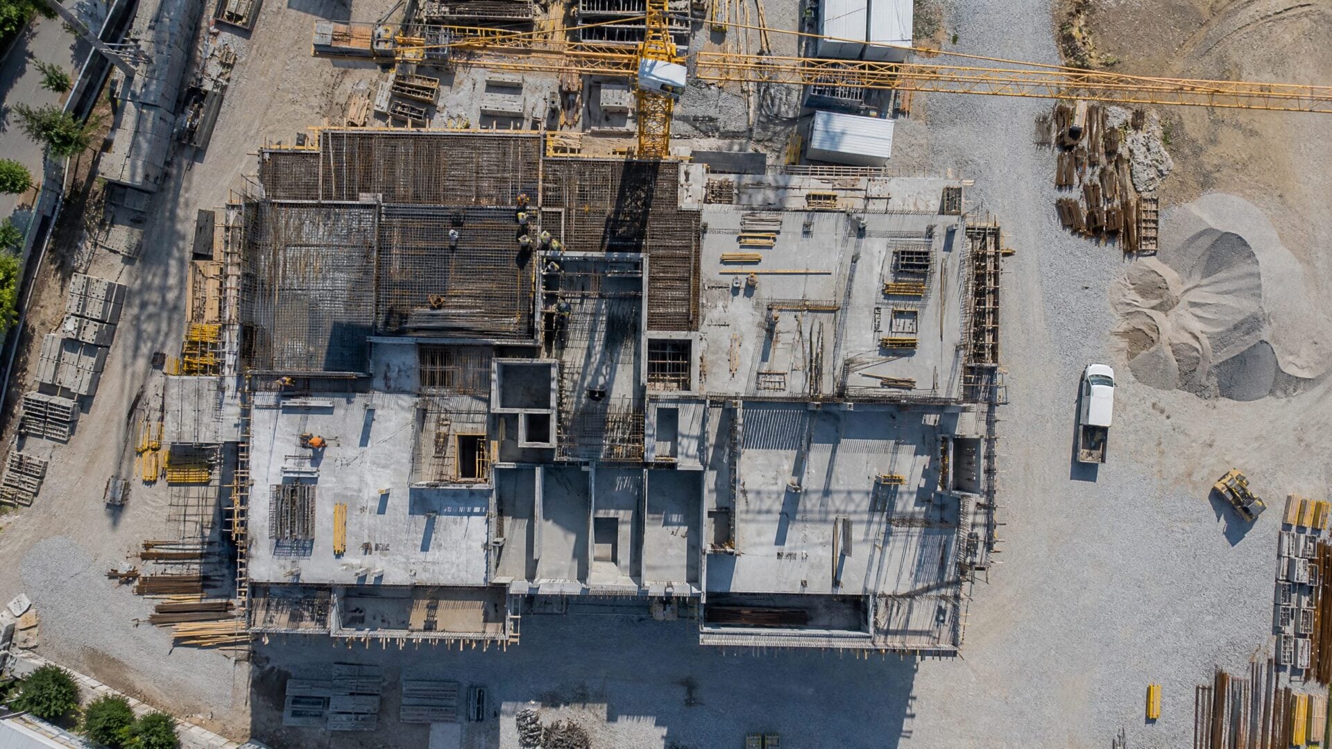 Aerial drone view of a commercial building under construction showing structural progress, materials, and stockpiles