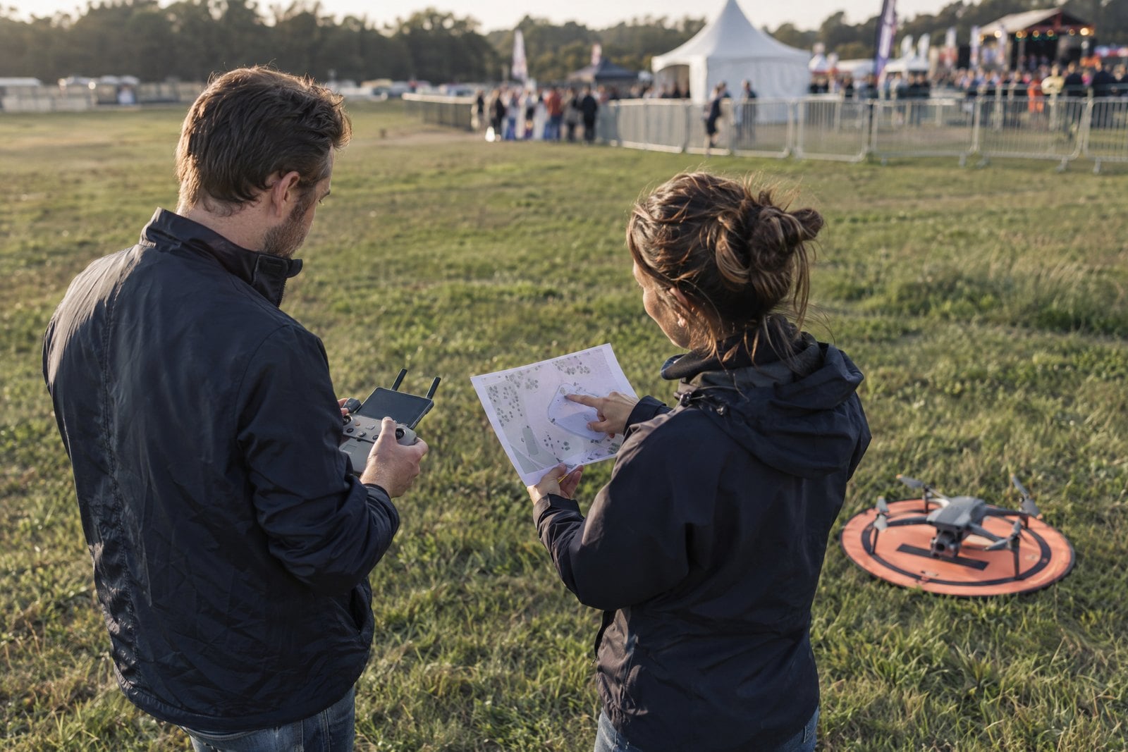 Two drone crew members review an event site plan from an empty perimeter launch area